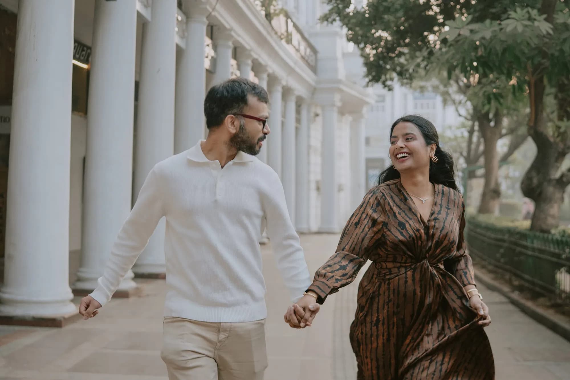 Couple running hand in hand along a white colonnade